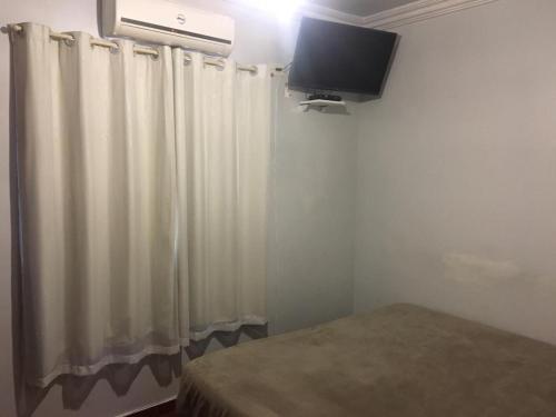 Pousada Castelo Branco في Arapongas: غرفة نوم مع ستارة بيضاء وتلفزيون