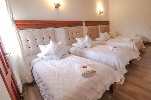 three beds in a room with white sheets and towels at Hotel las Palmas in Villa de Leyva