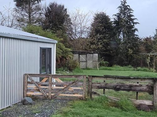 a wooden fence next to a building and a field at Marg's on the Corner in Kumara