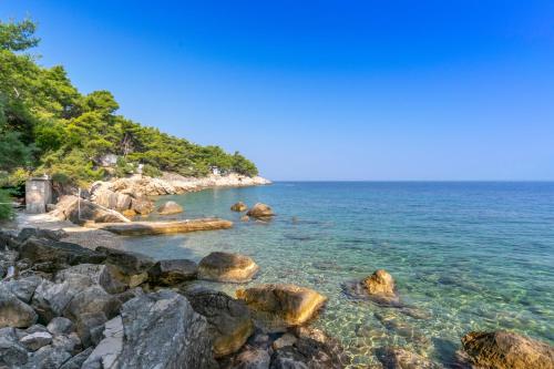 a beach with rocks and the water and trees at Holiday home Masha in Bogomolje