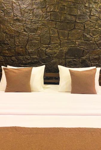 a bed with three pillows and a stone wall at Queens Mount Glen Heights in Nuwara Eliya