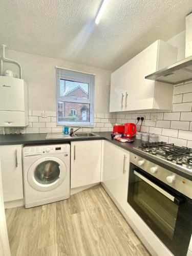 a kitchen with white cabinets and a washer and dryer at Central MK Home, Garden and Free Private Driveway Parking! 4 Beds Fully Equipped Train station 5 Mins in Milton Keynes