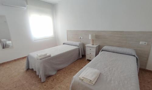 two beds in a white room with a window at Alojamientos Turísticos La Palmera in Cúllar-Vega
