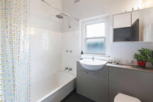 La salle de bains est pourvue d'une baignoire blanche, d'un lavabo et d'une baignoire. dans l'établissement Parkside Hideaway - Beautiful Art Deco near Zoo, à Melbourne