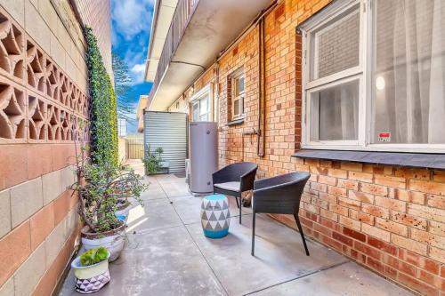 a patio with two chairs next to a brick wall at Adventure Awaits - Footsteps from West Beach in Adelaide
