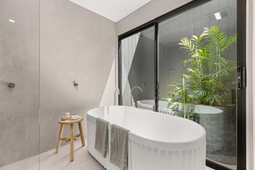 baño con bañera blanca y ventana grande en Thalassa Huskisson by Experience Jervis Bay en Huskisson