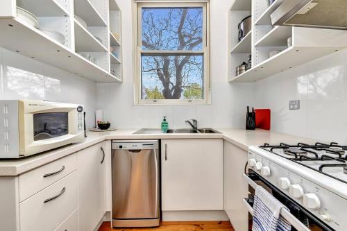 a white kitchen with a stove and a microwave at East Parklands Cottage - A Dreamy Garden Hideaway in Adelaide