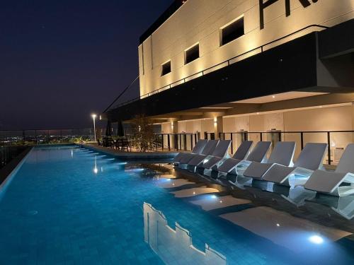 a swimming pool with white lounge chairs in front of a building at Vida Urbana - Zen - Setor Oeste in Goiânia