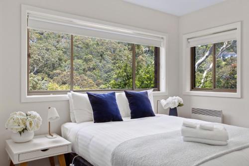 a bedroom with a white bed with blue pillows and two windows at The View 2 bed unit with stunning Hobart outlook in Hobart