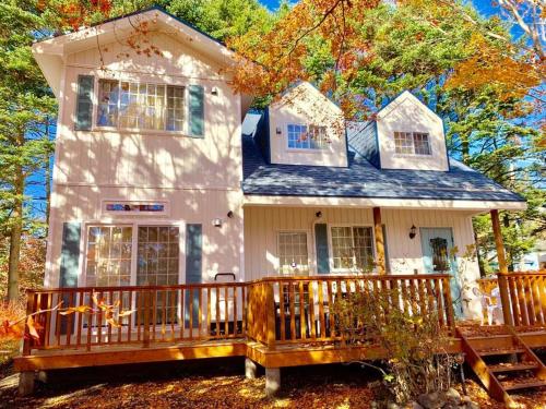 a small white house with a large wooden deck at 軽井沢ショッピングプラザ徒歩圏内の新築アメリカンハウス/ポーラーリゾート新軽井沢１ in Karuizawa