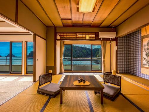 uma sala de estar com uma mesa, cadeiras e janelas em Yukai Resort Premium Koshinoyu em Nachikatsuura