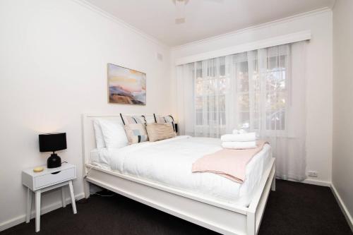 a white bedroom with a white bed and a window at Cranbrook Courtyard - A Sunny City-fringe Retreat in Wayville