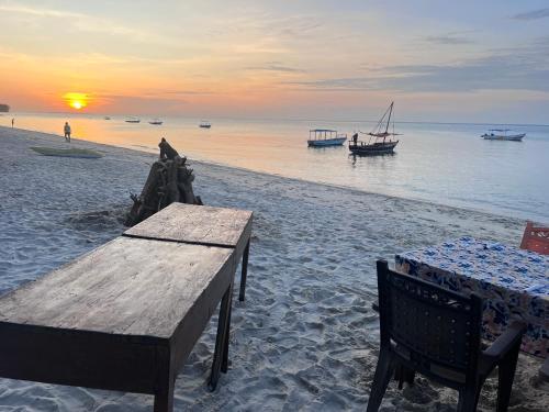 Maweni CoralBay Beach Villa في كيليندوني: طاولة وكراسي على شاطئ مع غروب الشمس