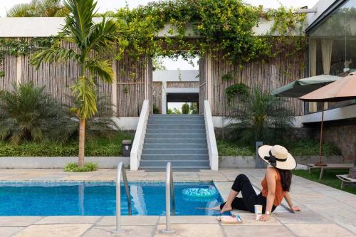 Dos mujeres están sentadas junto a una piscina. en Open House by StayVista - Nestled in nature, featuring a Swimming pool & Expansive lawn for a serene retreat, en Shikrapur