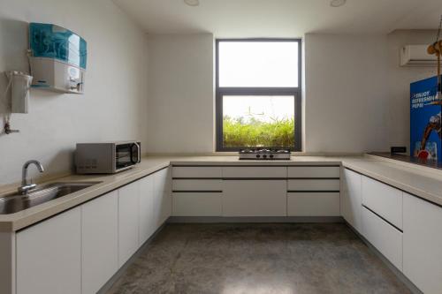 a white kitchen with a sink and a window at Open House by StayVista - Nestled in nature, featuring a Swimming pool & Expansive lawn for a serene retreat in Shikrapur