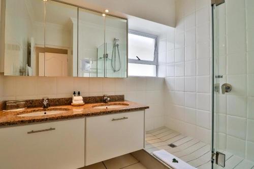 a bathroom with two sinks and a glass shower at Hermanus Beachfront Lodge - Solar Power in Hermanus