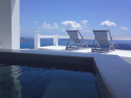 two chairs sitting on the edge of a swimming pool at Altana Cliffside Villas in Imerovigli