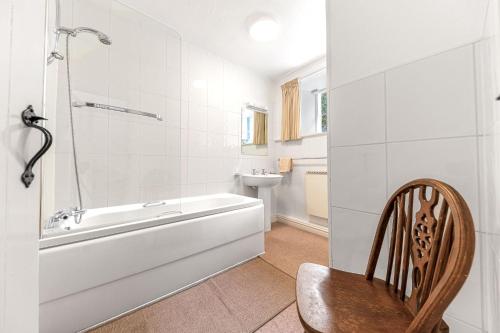 a bathroom with a tub and a toilet and a chair at The Sheiling, Traditional Lakeland Cottage, Coniston in Coniston