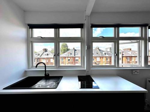 a kitchen with three windows and a sink and a counter at Cozy Studio near Regent’s Park N9 in London