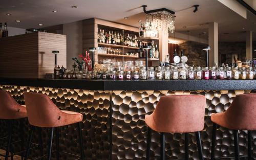 un bar avec trois tabourets devant un comptoir dans l'établissement Excelsior Dolomites Life Resort, à San Vigilio Di Marebbe