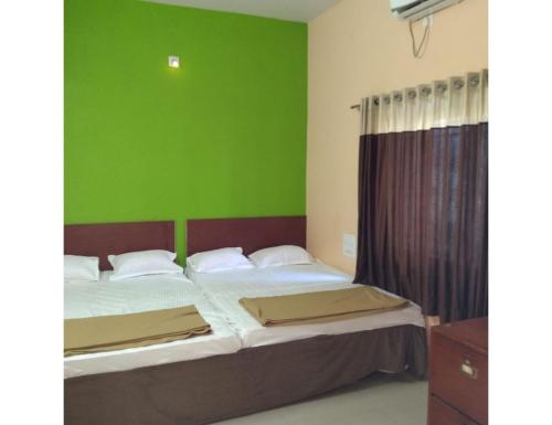Hotel Shree, Somnath في سومناث: غرفة نوم بسريرين وجدار أخضر