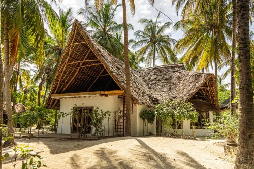 uma casa com telhado de palha e palmeiras em Kinazi Upepo Beach Eco Lodge em Paje