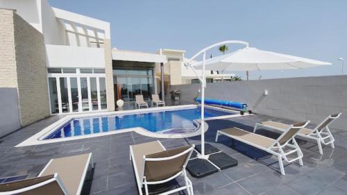 阿德赫的住宿－Villa Elisabetta, Luxury Villa with Heated Pool Ocean View in Adeje, Tenerife，一个带椅子和桌子的游泳池以及一把遮阳伞