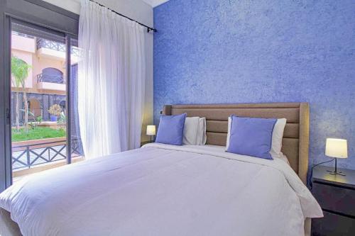 a bedroom with a large bed with blue walls and a window at Les Jardins Sakar - Marrakech - Deux Chambres Exceptionnelle in Marrakech