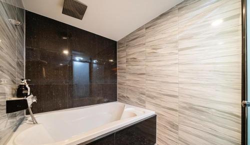 a bathroom with a white tub and a tile wall at Tomoto Hotel in Incheon