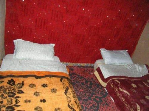 - une chambre avec 2 lits et un mur rouge dans l'établissement ATFIL CAMP, à M'Hamid El Ghizlane