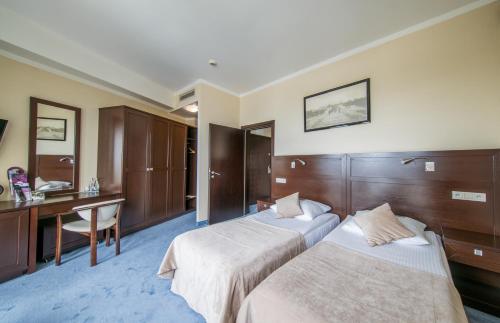 a hotel room with two beds and a desk at Hotel Aurora Family & SPA in Międzyzdroje