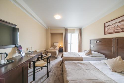a hotel room with two beds and a desk at Hotel Aurora Family & SPA in Międzyzdroje