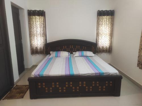 a bedroom with a bed with a striped comforter and two windows at Krishna Serviced Apartment in Kalasa