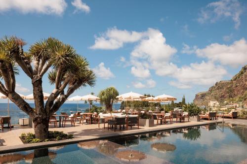 a pool at a resort with tables and chairs at Saccharum - Resort and Spa - Savoy Signature in Calheta