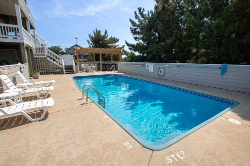 a large swimming pool with chairs and a house at Oceanside, Private Pool, Hot Tub, Community Pool, CD7, Sandfiddler Lodge in Duck