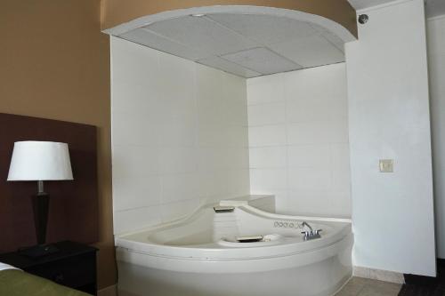 American Inn & Suites في وترفورد: غرفة بيضاء مع سرير وحوض استحمام