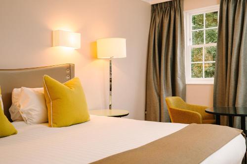 a hotel room with a bed with yellow pillows and a window at Royal Berkshire in Ascot