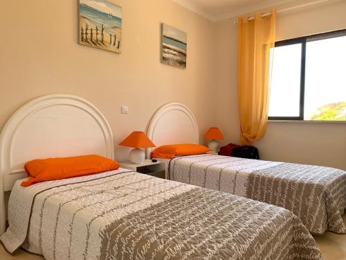 1 dormitorio con 2 camas con almohadas de color naranja y ventana en Ver-O-Mar en Carvoeiro