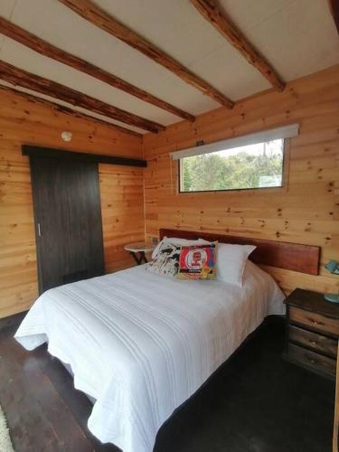 um quarto com uma cama branca num chalé de madeira em Mountain Glamping - Nature and Relax em Fúquene