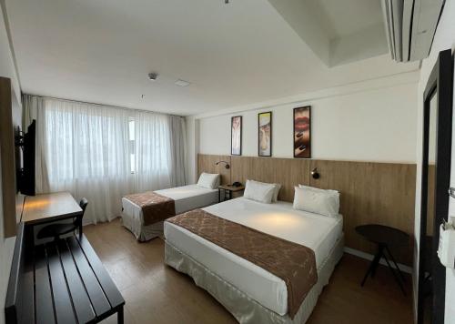 a hotel room with two beds and a desk at Transamerica Executive Maringá in Maringá