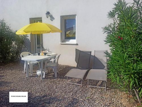 une table et des chaises blanches avec un parapluie jaune dans l'établissement Studio Quiétude, à Saint-Aygulf