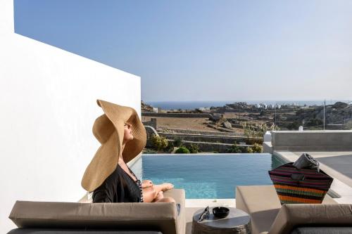 a person wearing a hat sitting in a chair next to a pool at Villa Evi & Suites in Mikonos