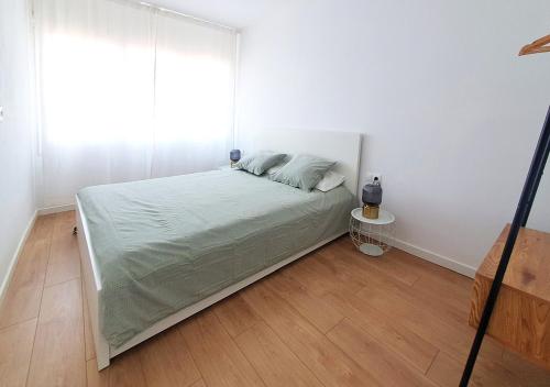 een witte slaapkamer met een bed en een houten vloer bij Acojedor piso cerca del metro in Cornellà de Llobregat