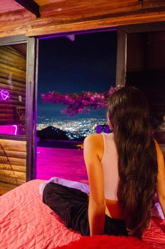 a woman sitting on a bed looking out a window at Romero Glamping y Cabañas in Cali