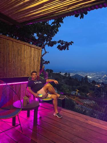 a man sitting on a bench on a deck with purple lights at Romero Glamping y Cabañas in Cali