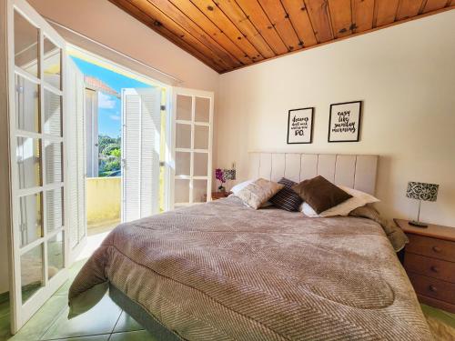 a bedroom with a large bed and a large window at Quatro Estacoes Hospeda -Vila 01 , sua casa em Campos do Jordao, a 1 km do centro turistico in Campos do Jordão