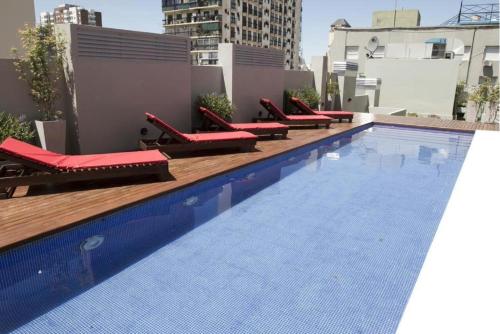 a large swimming pool with red lounge chairs on a building at Monoambiente Frente Al Hospital Italiano in Buenos Aires