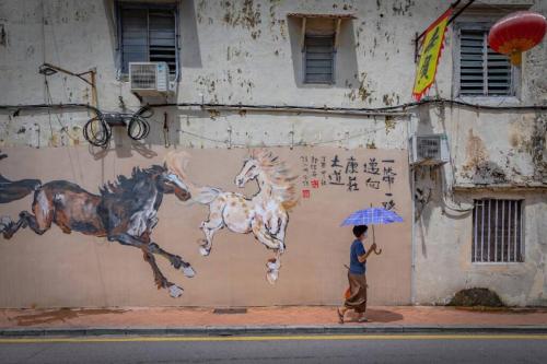 a man with an umbrella standing next to a wall with a painting of horses at LEJU 21 樂居 Explore Malacca from a riverside house in Melaka