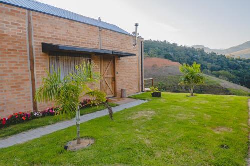 a brick building with a yard with palm trees at Pousada Ho'oponopono Chalets & Wine in Sapucaí-Mirim