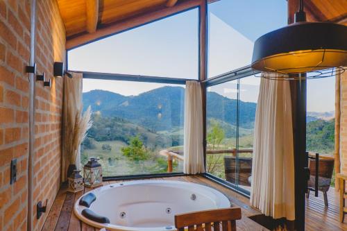 a bath tub in a room with a large window at Pousada Ho'oponopono Chalets & Wine in Sapucaí-Mirim